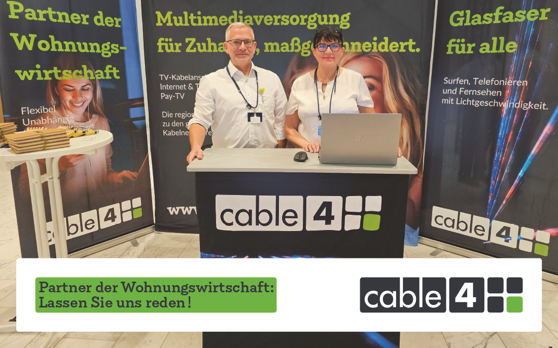 Zwei Cable4-Mitarbeitende am Messestand mit Laptop vor Bannern zu Multimedia-Versorgung, Glasfaser und Partnerschaft in der Wohnungswirtschaft.